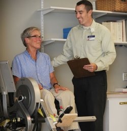 A researcher from the Marcus Institute for Aging Research in Boston, MA stands next to an older woman who is seated on a piece of exercise equipment.